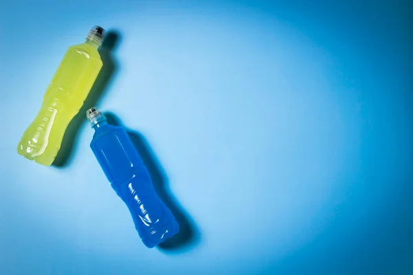 Deux bouteilles en plastique avec énergie isotonique bleu et jaune boisson sportive transparente sur fond bleu clair. Vue du dessus, espace de copie — Photo