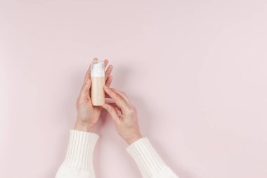 Kadın eli jöle, yüz kremi, CC, BB yüz kremi toneri için kozmetik şişesi tutuyor. Makyaj malzemesi ise pastel pembe arka plan üzerine. Boş plastik paket kabı metin için yer ile taklit