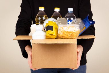 Kadın eli, market ürünleriyle dolu bir karton kutu tutuyor. Gönüllü bağış kutusuna yiyecek topluyor. Bağış, yardım, gıda bankası, yoksul ailelere, göçmenlere, mültecilere yardım
