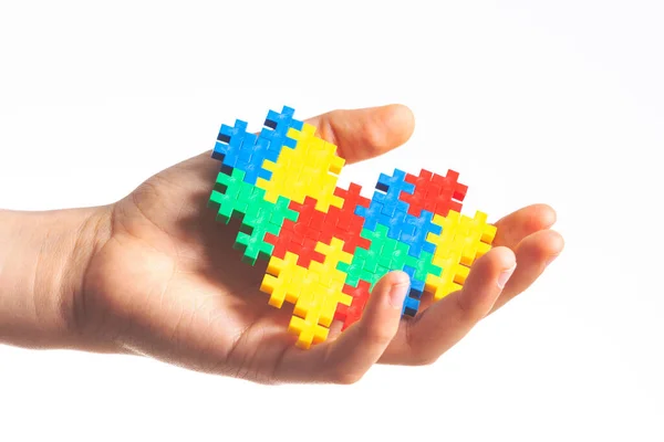 Kinderhände mit buntem Puzzle-Herz auf weißem Hintergrund. Konzept zum Welt-Autismus-Tag — Stockfoto