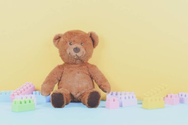 Bebek çocuklar oyuncak arka planda kahverengi oyuncak ayı ve renkli yapı taşları ile pastel sarı ve mavi arka planda tuğlalar. Ön görünüm