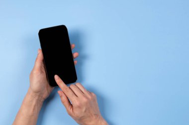 Kadın eli akıllı telefon ekranına dokunuyor ve açık mavi arkaplanda boş cep telefonu ekranında işaret ediyor.