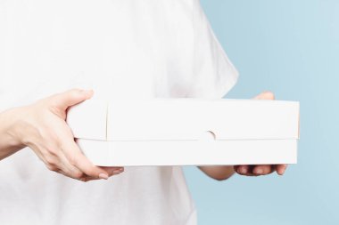 Kadın elleri açık mavi arka planda beyaz karton kutu tutuyor. Mokup paket kutusu. Paketleme, alışveriş, teslimat konsepti