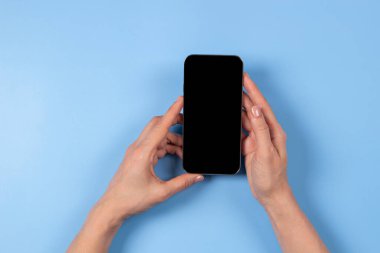 Açık mavi arka planda akıllı telefonu tutan kadın.