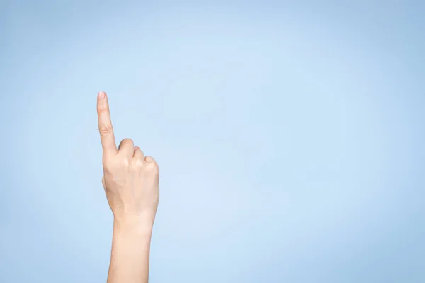 Die weibliche Hand zeigt die Nummer eins. Frau zeigt mit Zeigefinger auf hellblauen Hintergrund — Stockfoto