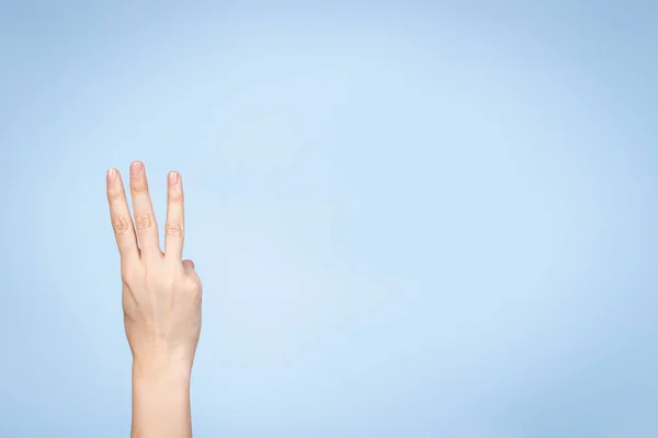 La mano femenina muestra el número tres. Mano de mujer mostrando tres dedos, señalando los dedos hacia arriba sobre fondo azul claro — Foto de Stock