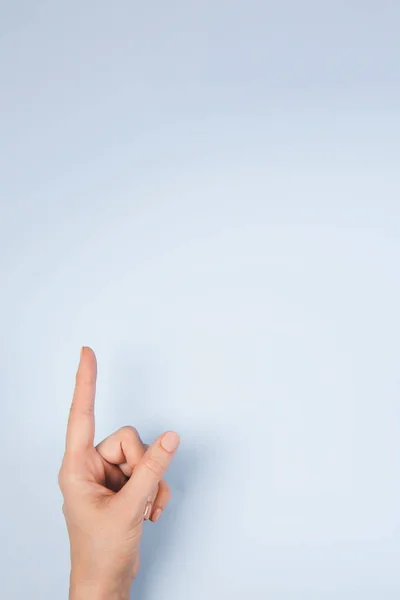 Frauenhand zeigt mit Zeigefinger nach oben auf etwas Virtuelles und Unsichtbares, Kopierraum auf hellblauem Hintergrund — Stockfoto