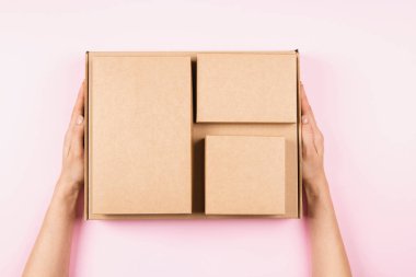 Üst kattan kadın ellerine karton kutular yığılıyor. Pastel pembe arka planda boş kahverengi paket kutuları. Paketleme, alışveriş, ücretsiz nakliye, teslimat konsepti