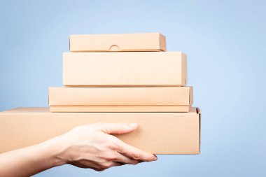 Kadın ellerinde bir yığın karton kutu. Açık mavi arka planda boş kahverengi paket kutuları. Paketleme, alışveriş, ücretsiz nakliye, teslimat konsepti