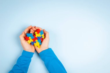 Çocuk eli açık mavi arka planda renkli yapboz kalbini tutuyor. Dünya otizm farkındalık günü konsepti