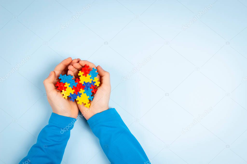 Child hand holding colorful puzzle heart on light blue background. World autism awareness day concept