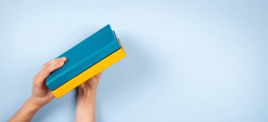 Açık mavi arkaplan üzerinde iki mavi ve sarı renkli kitabı tutan kadın eller. Eğitim, kendi kendini öğrenme, kitap değişimi