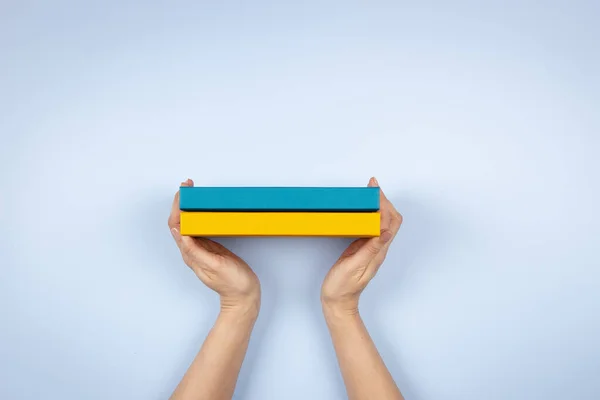 Female hands holding two blue and yellow color books over light blue background. Education, self-learning, book swap