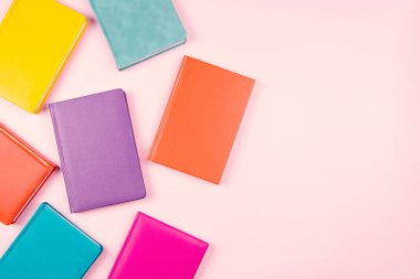 Pastel pembe arka plan üzerine renkli ciltli kitaplar. Üst görünüm, metin için boşluk kopyala