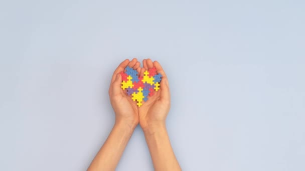 Всесвітній день аутизму концепція обізнаності. Жінка і дитячі руки тримають серце-головоломка на світло-блакитному тлі. Вид зверху — стокове відео