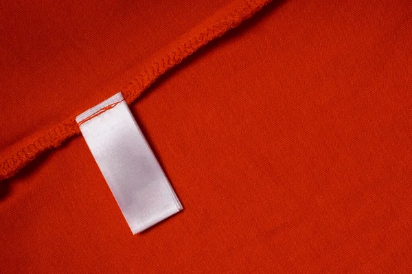 Bílé prázdné prádlo péče oblečení štítek na červeném textilním pozadí textury. Horní pohled — Stock fotografie