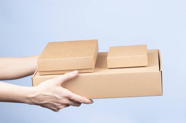 Kadın ellerinde bir yığın karton kutu. Açık mavi arka planda boş kahverengi paket kutuları. Paketleme, alışveriş, ücretsiz nakliye, teslimat konsepti