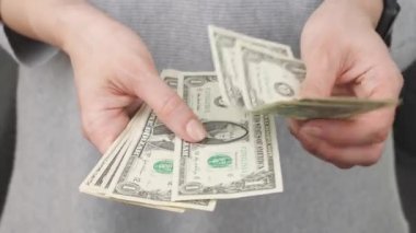 Kadın eli, nakit Amerikan doları banknotlarını sayıyor. Kadın elini uzatıyor, birkaç dolarlık banknot veriyor ve kendisine birkaç dolar bırakıyor. Nakit ödeme, tasarruflar, faturalar, vergiler, aile bütçesi