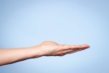 Kadın el hareketi. Açık mavi arka planda elini açık tutan bir kadın. Avuç içi boşluğu bir şey tutuyormuş gibi duruyor. Ön görünüm