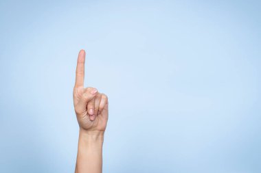 El hareketi. Kadın eli bir numarayı gösteriyor. Açık mavi arkaplanda işaret parmağı olan bir kadın