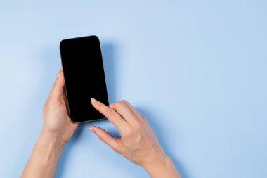 Kadın eli akıllı telefon ekranına dokunuyor ve açık mavi arkaplanda boş cep telefonu ekranında işaret ediyor.