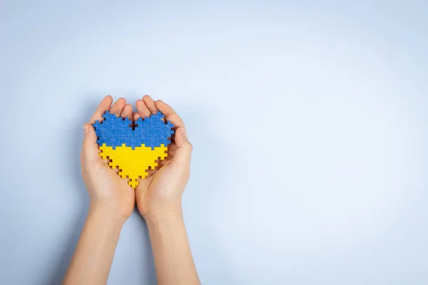 Детские руки, держащие флаг Украины, раскрашивают сердце на светло-голубом фоне. Вид сверху — стоковое фото