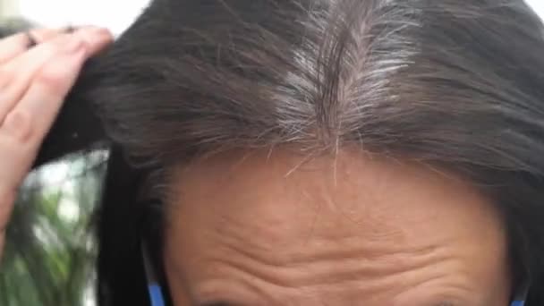 Orta yaşlı bir kadın gri saç kökleriyle koyu renk saçlarına dokunuyor. Saçları ağarmış, saçları dökülmüş. Kapat. — Stok video