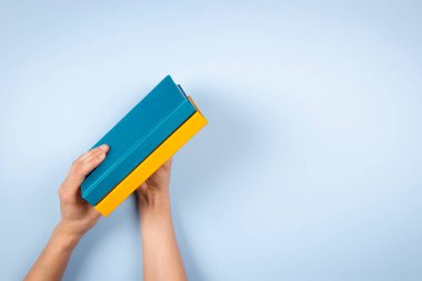 Açık mavi arkaplan üzerinde iki mavi ve sarı renkli kitabı tutan kadın eller. Eğitim, kendi kendini öğrenme, kitap değişimi