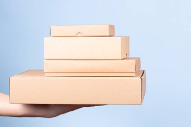 Kadın ellerinde bir yığın karton kutu. Açık mavi arka planda boş kahverengi paket kutuları. Paketleme, alışveriş, ücretsiz nakliye, teslimat konsepti