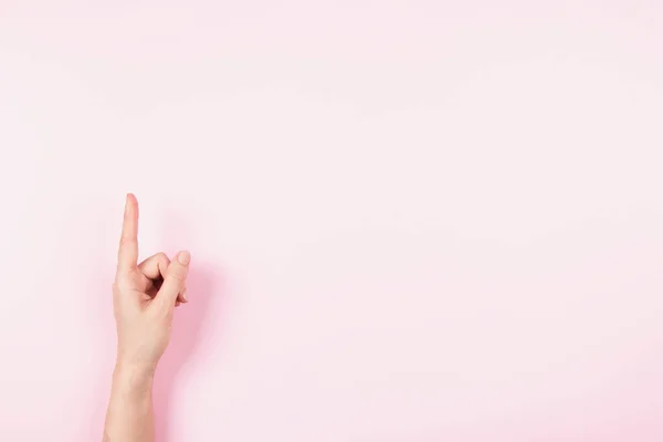 Woman hand pointing up with index finger to something virtual and invisible, copy space on pastel pink background. Hand gesture, number one — Foto de Stock