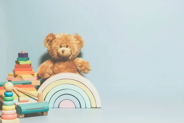 Kids toys collection. Teddy bear, wooden pyramid tower, rainbow color xylophone and baby toys on light blue background. Front view