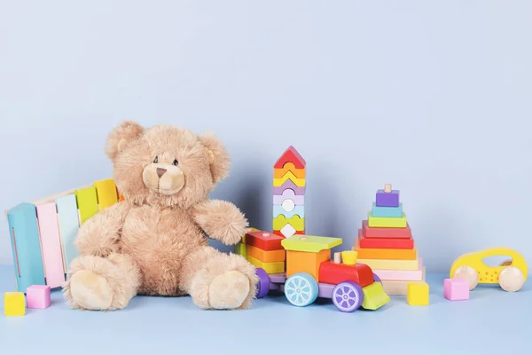 Educational kids toys collection. Teddy bear, wooden train, rainbow color xylophone and baby toys on light blue background. Sustainable, eco-friendly toys. Front view