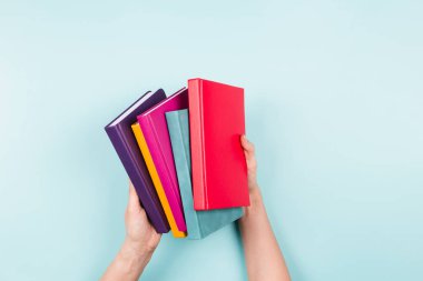 Açık mavi arkaplan üzerinde kitap yığını tutan kadın eller. Eğitim, kendi kendine öğrenme, hobi, evde dinlenme zamanı.