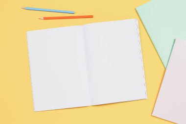 Sarı arkaplanda boş defterleri ve renkli kalemleri aç. Üst görünüm