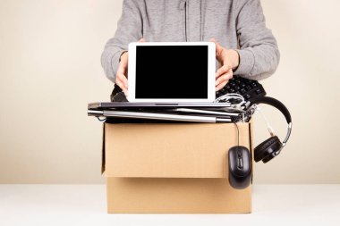 Kadın elleri dijital tableti tutuyor. Kullanılmış bilgisayarlarla, telefonlarla, geri dönüşüm için aletlerle dolu bir karton kutu. Yeniden kullanım ve geri dönüşüm konsepti için planlanmış eskitme, e-atık, bağış, elektronik atık