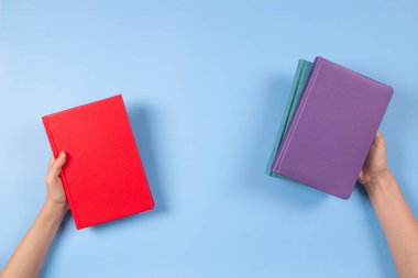 Açık mavi arka planda kitapları tutan eller. Eğitim, kendi kendini öğrenme, kitap değişimi, paylaşma, kitap çapraz kavramı