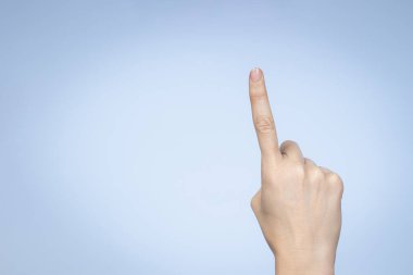 El hareketi. Kadın eli bir numarayı gösteriyor. Açık mavi arkaplanda işaret parmağı olan bir kadın.