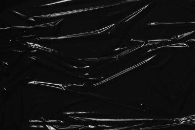 Siyah arka planda şeffaf plastik ambalaj. Buruşmuş plastik selofan kırışıklığı. Plastik yüzeydeki kıvrımlara ve kıvrımlara ışığı ve gölgeyi yansıtıyor. Doku kaplama efekti şablonu.