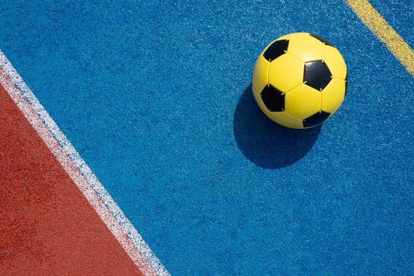 Colorful sports court background. Light blue and red field rubber ground with white line and yellow soccer ball on sunny day outdoors. Top view