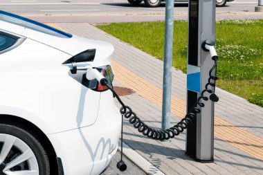 Şarj olan gri elektrikli arabaya takılan güç kaynağını kapatın. Elektrikli araba şarjı için güç kaynağı. Şehirde elektrikli araba şarj istasyonu var..