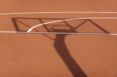Güneşli bir günde turuncu basketbol sahası üzerinde kalkan ve basketbol yüzüğü olan rafın gölgesi. Basketbol oyunu arka planı.