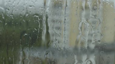 Şiddetli yağmurda nemli camlara damlayan yağmur damlacıkları şehrin yüksek katlı evlerinin gölgeleriyle bulanık arka planda kalıyor.