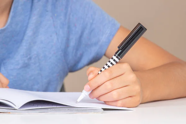 Kid holding pen in left hand and doing homework, writing in open notebook. Left Handers Day.