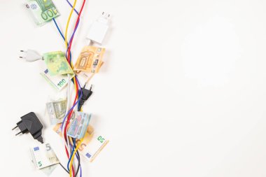 Elektrik kabloları, üzerinde Euro banknotları olan kabloları beyaz arka planda büküyor. Enerji verimliliği, enerji tüketimi, elektrik maliyeti ve pahalı enerji kavramı.