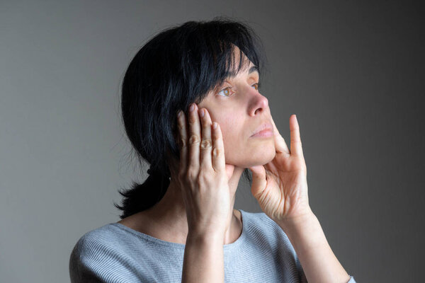 Face yoga, facial gymnastics, daily self care routine. Middle age caucasian woman performing facial exercises at home.