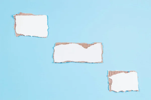 Three pieces of white corrugated cardboard with torn edges on light blue background. Top view, copy space.