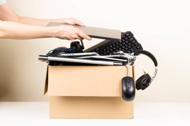 Woman hands put old laptop computer in cardboard box full used computers and gadget devices for recycling. Planned obsolescence, e-waste, donation, electronic waste for reuse and recycle concept.