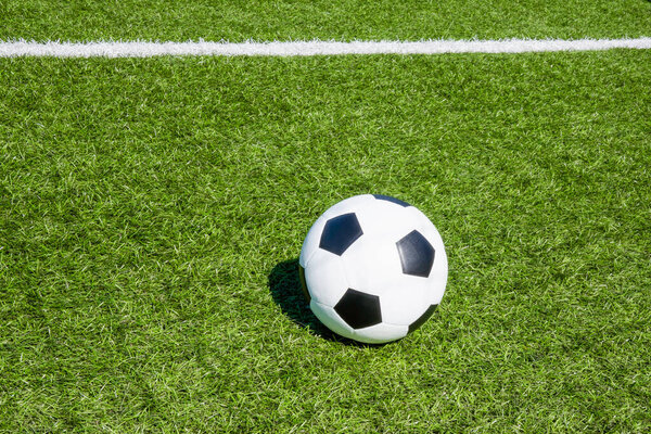Football soccer sport background. Green artificial turf soccer field with white line, shadow from football goal net and soccer ball on sunny day outdoors. Top view.
