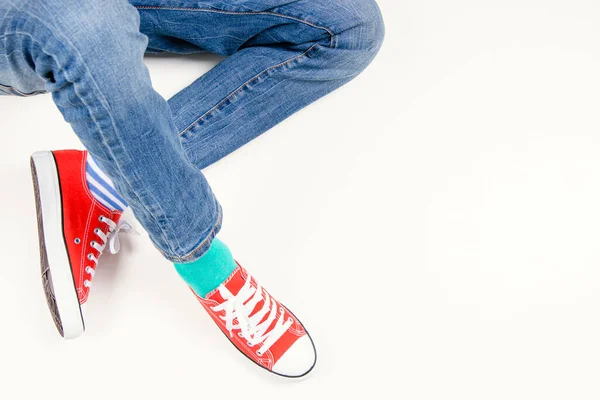 Farklı çorap giyen bir çocuk. Uyumsuz çoraplar içinde çocuk ayakları ve beyaz arka planda oturan kırmızı spor ayakkabılar. Çorap Günü, Zorbalık Karşıtı Hafta, Down Sendromu Farkındalık Konsepti.