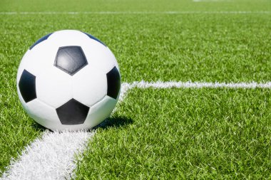 Soccer ball on green synthetic artificial grass soccer sports field with white corner stripe line.